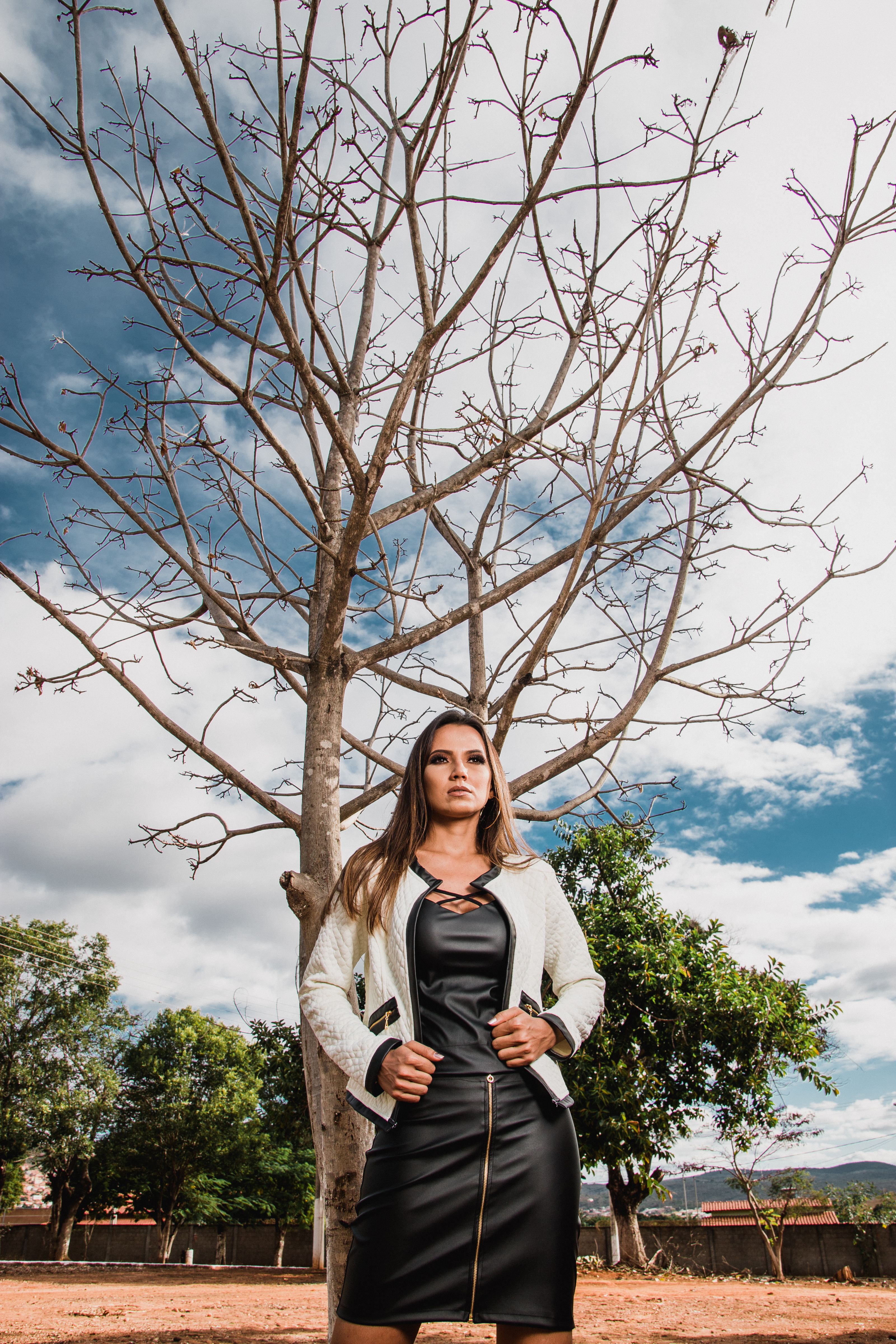 Uma mulher fica confiante sob uma árvore sem folhas, exibindo moda e beleza natural.