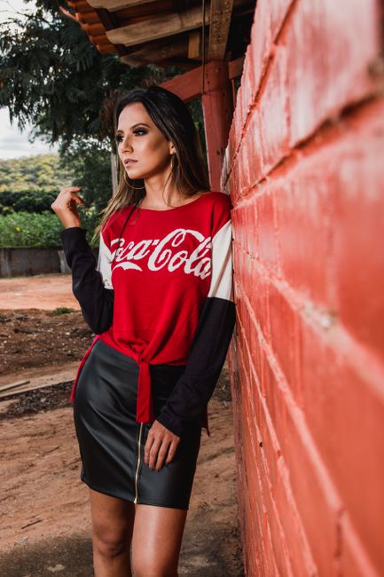 Fashionable woman in a Coca-Cola shirt poses against a red brick wall outdoors.
