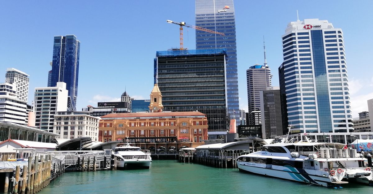 Vibrant Auckland cityscape featuring waterfront, skyscrapers, and yachts under a clear blue sky.