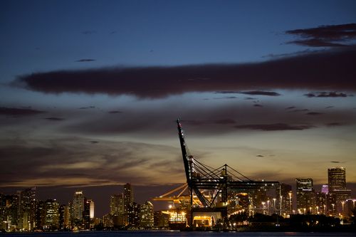 Free Twilight cityscape of a harbor with crane and illuminated skyline against a sunset sky. Stock Photo