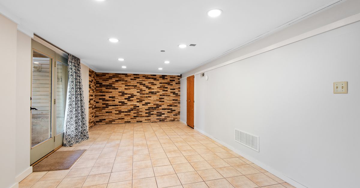 Bright and empty basement with brick accent wall and tile flooring.
