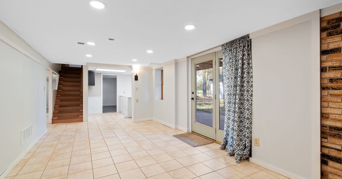 Bright and empty basement with tile flooring and glass doors leading outside.