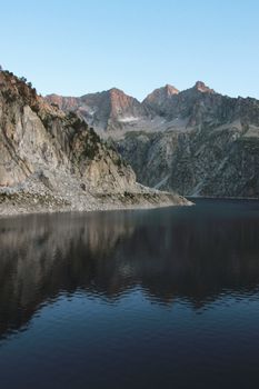 Calm lake reflecting rugged mountain range in Aragnouet, Occitanie. Perfect for travel enthusiasts.
