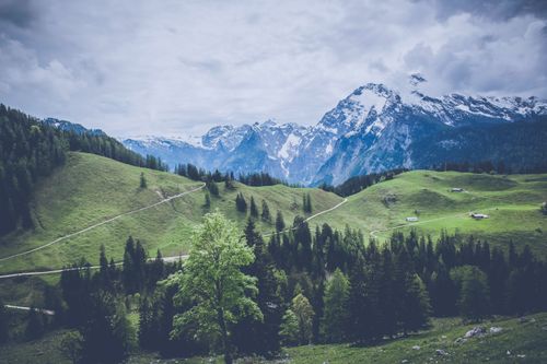 Free Breathtaking view of a lush green valley and snow-capped mountains under a cloudy sky. Stock Photo