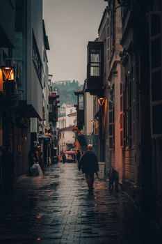 A person walking down a narrow, moody alley in Izmir, Turkey, showcasing rich architectural details.