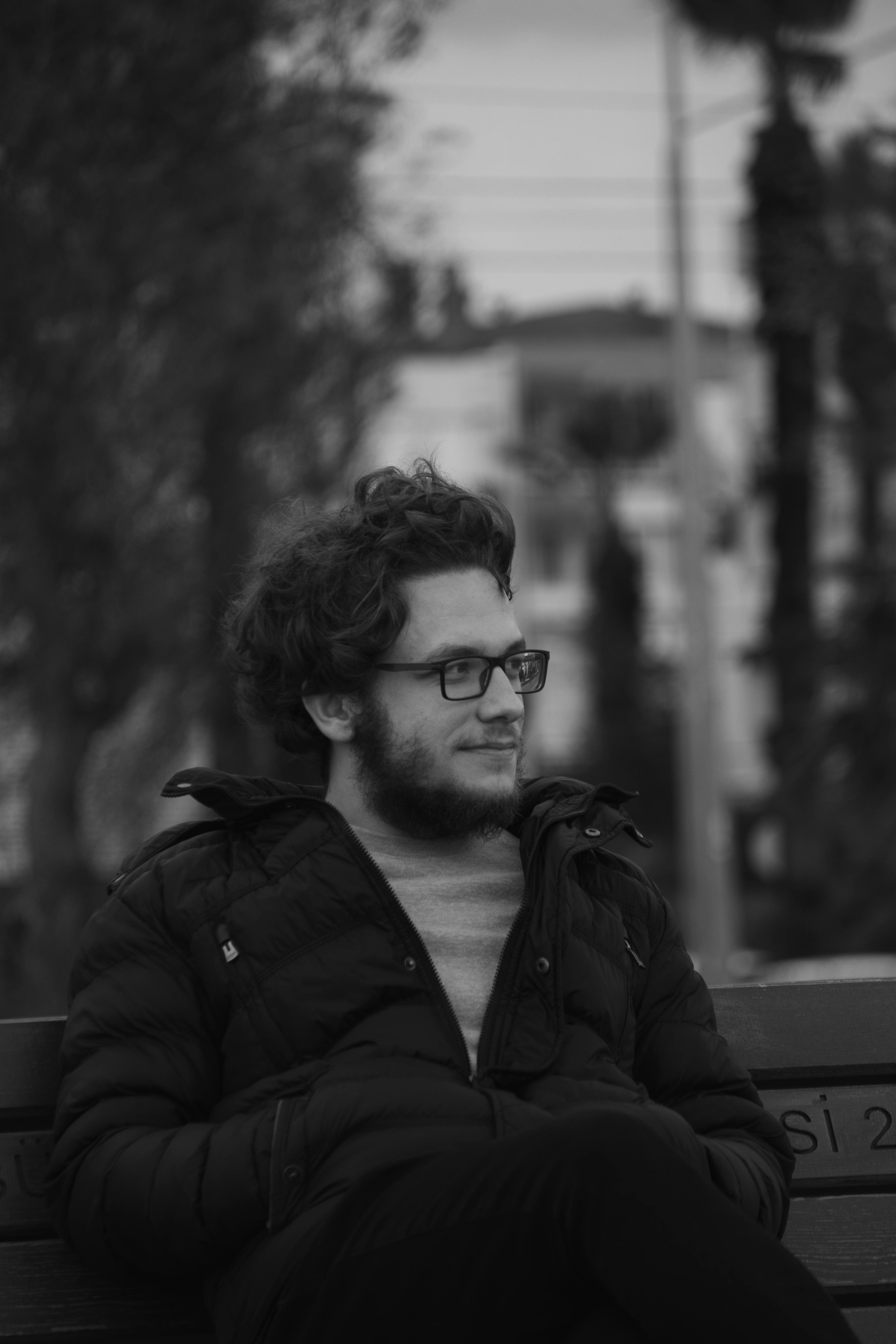 A man in winter attire sitting on a bench in a monochrome setting.