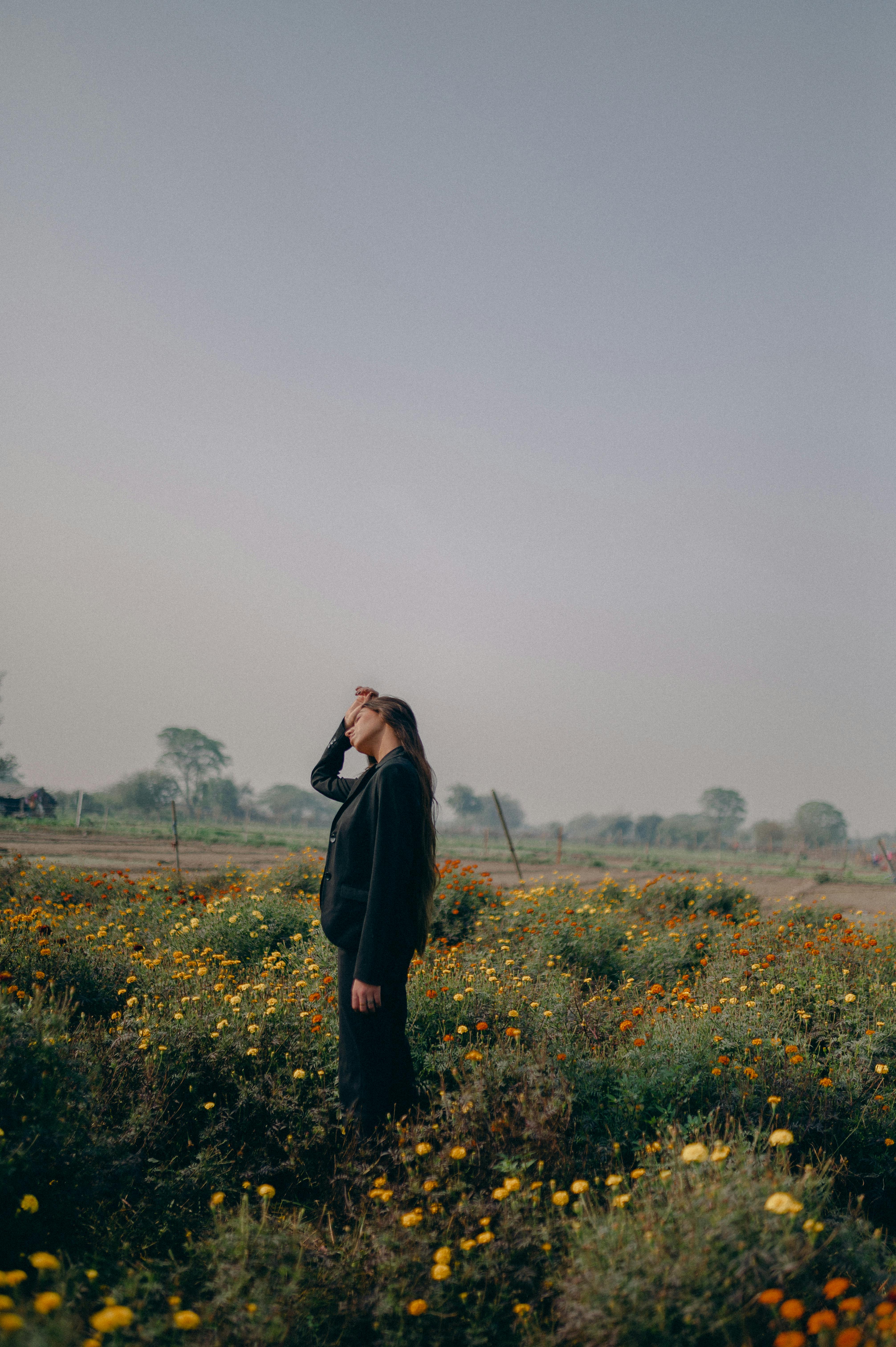 A woman stands in a meadow of wildflowers in New Delhi, India, under a clear sky.