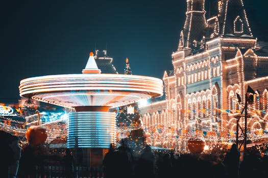 Long exposure of a brightly illuminated amusement park ride with festive lights and a historic building backdrop.