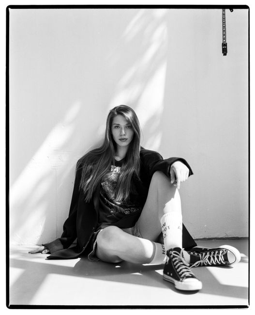 Black and white portrait of a woman sitting casually with long hair and sneakers.