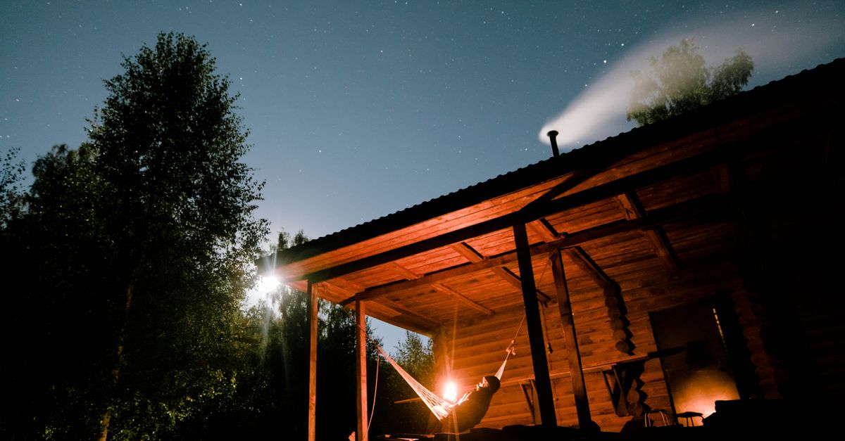 A wooden cabin in a misty forest with a hammock and a book on a blanket