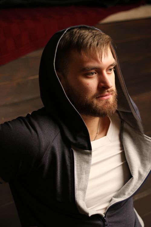 Free Young man in a stylish black hoodie posing thoughtfully indoors with natural lighting. Stock Photo