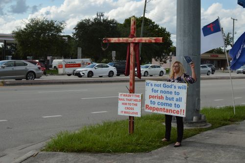 Free Woman holds religious sign on roadside advocating repentance with cross nearby. Stock Photo