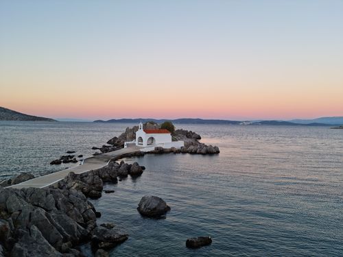 Free Scenic view of a coastal chapel at sunset with calm seas in Sikiada, Greece. Stock Photo