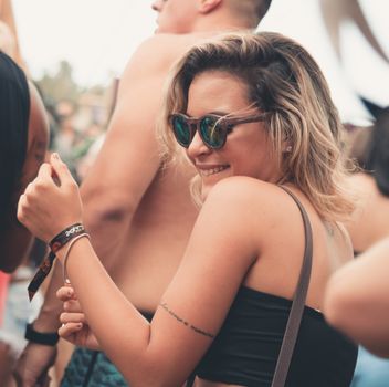 A stylish young woman with sunglasses smiling at an outdoor festival.