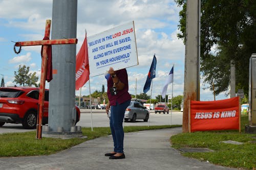 Woman Holding a Religious Signboard on Sidewalk