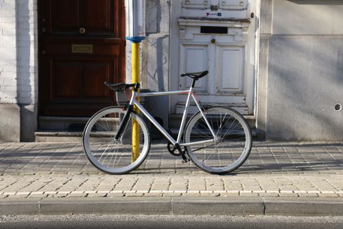 Free A silver fixie bicycle parked on a city sidewalk in sunlight. Stock Photo