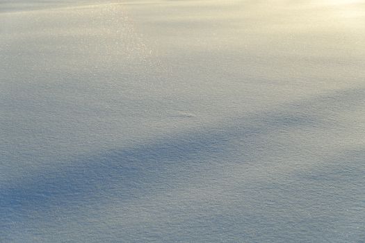 A tranquil snowy landscape with a warm sunrise glow casting shadows on the surface.