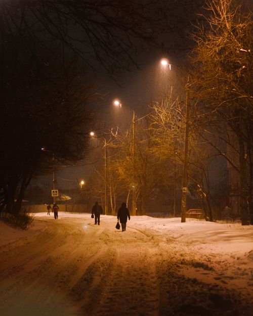 Free A peaceful winter night scene in Ukraine with people walking along a snow-covered street under lamp lights. Stock Photo