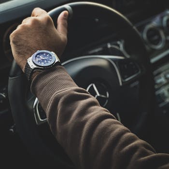 Close-up of a hand wearing a watch while holding a car steering wheel.