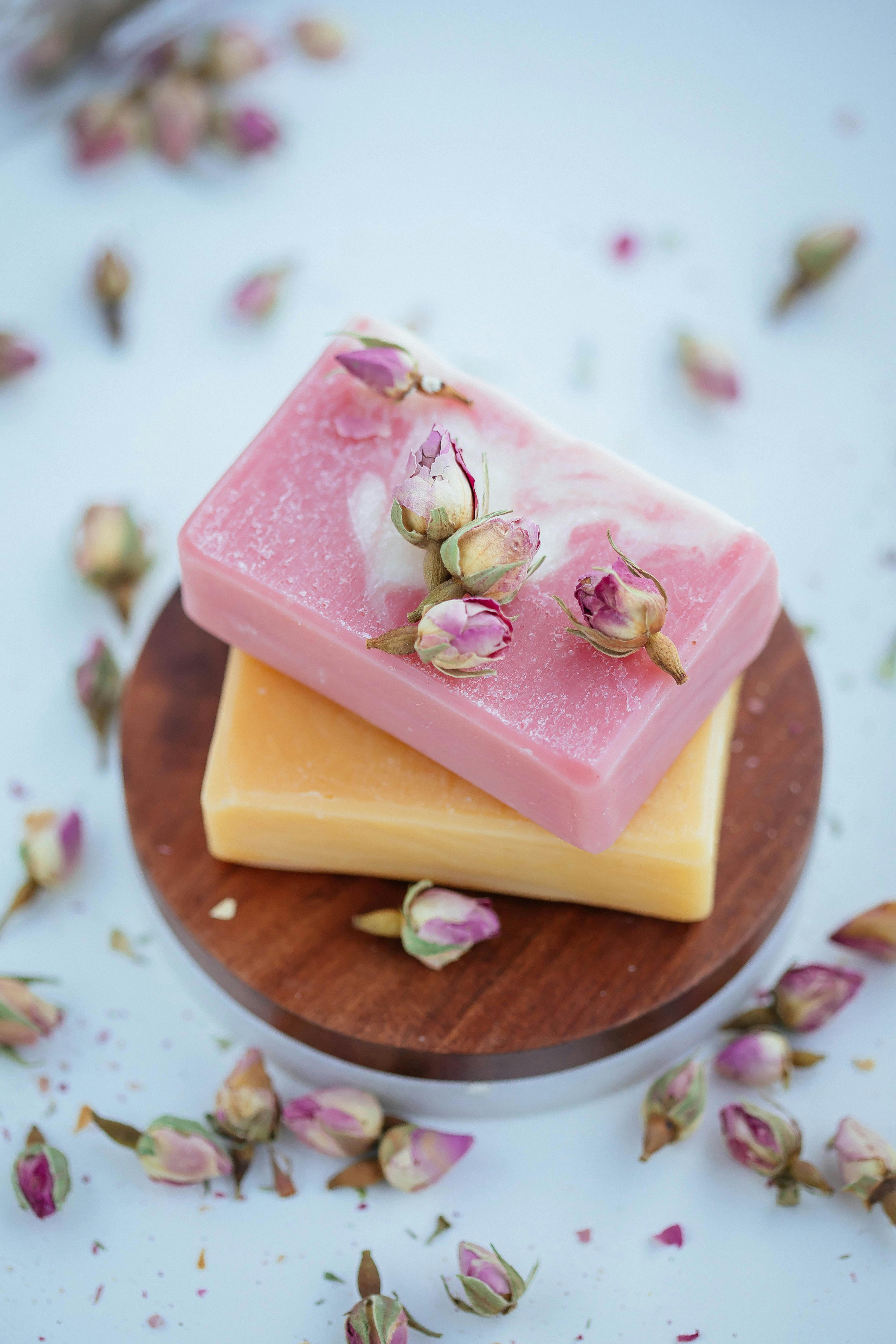 Close-up of two handmade soaps adorned with rosebuds, resting on wooden dish.