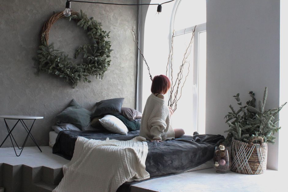 A serene bedroom scene with a woman sitting on a bed, gazing out the window.