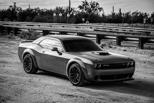 Grayscale Photo of Dodge Challenger Parked on Unpaved Road