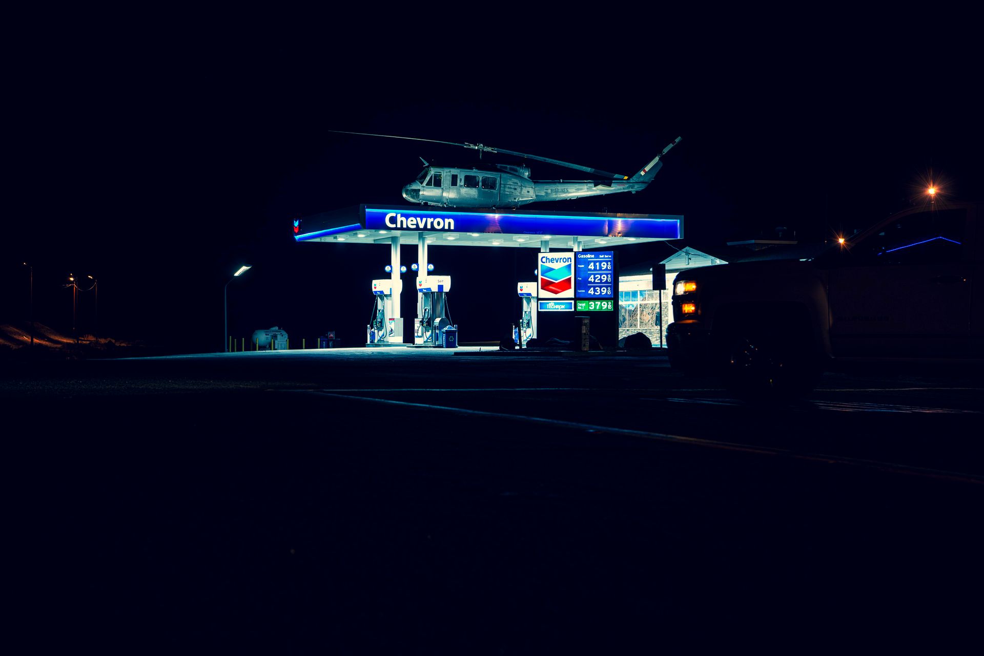 A helicopter hovering above a lit Chevron gas station during nighttime, creating a unique urban scene.
