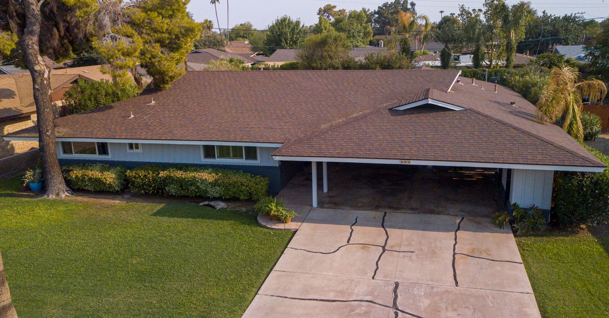 Aerial view of a suburban house with a brown roof surrounded by greenery.