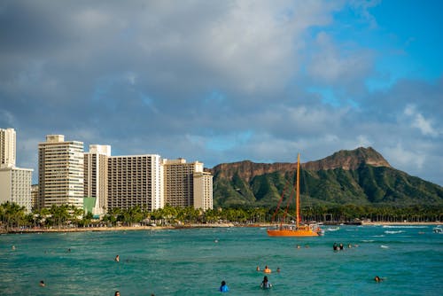 People Swimming on Ocean near Green and Brown Mountain