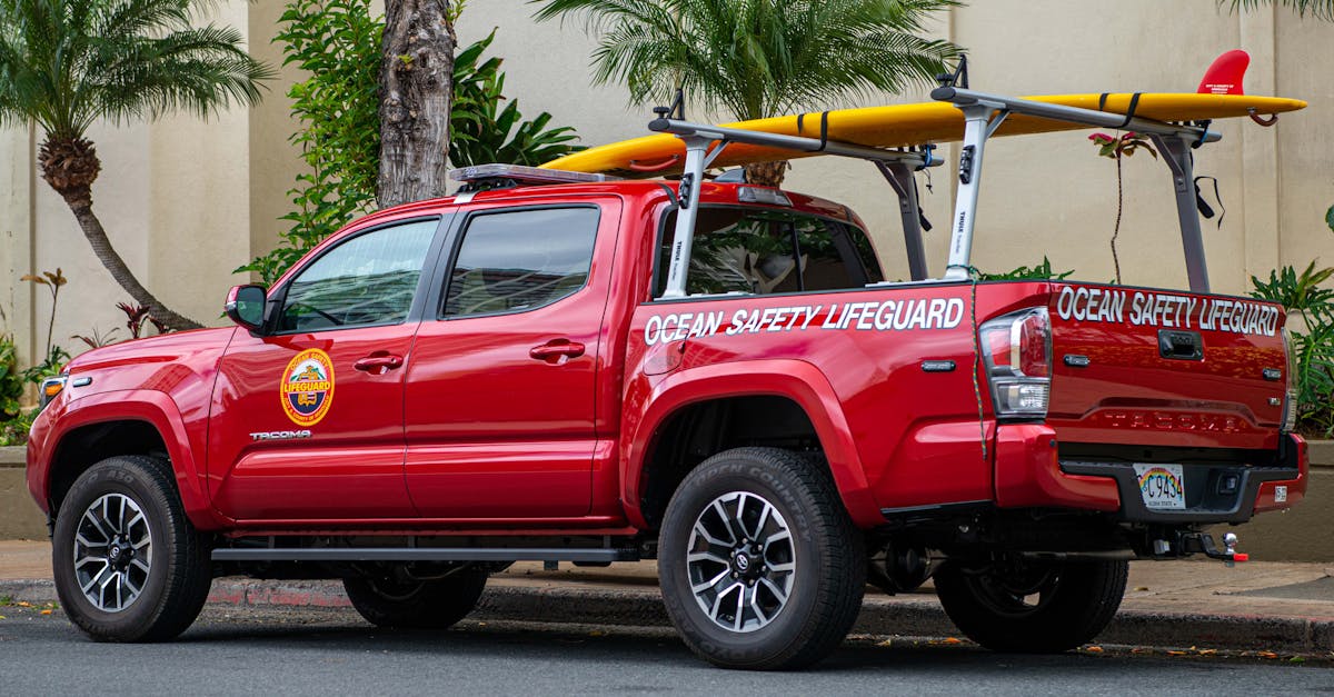 Photo by Derwin Edwards A red lifeguard pickup truck equipped with a surfboard, parked on a city street with palm trees.