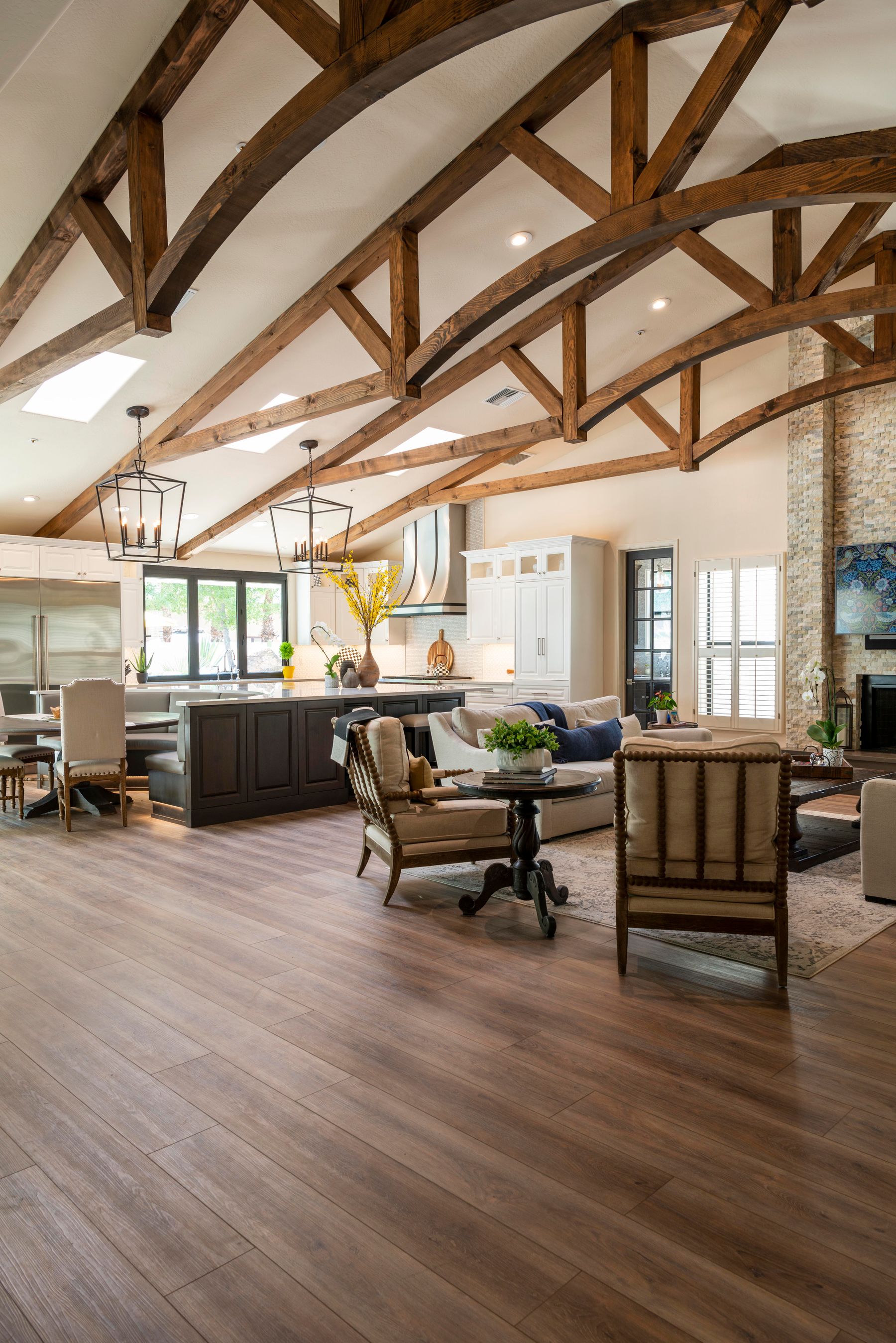 Spacious open-plan living and kitchen area with wooden flooring continuing under tables and seating