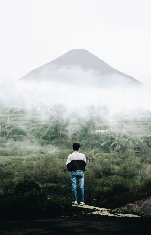 Free A man stands on a ledge, gazing at a mist-covered mountain, capturing the serene Indonesian landscape. Stock Photo