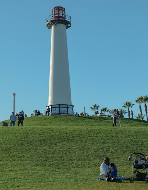 People on Green Grass Field Near Lighthouse Under Blue Sky