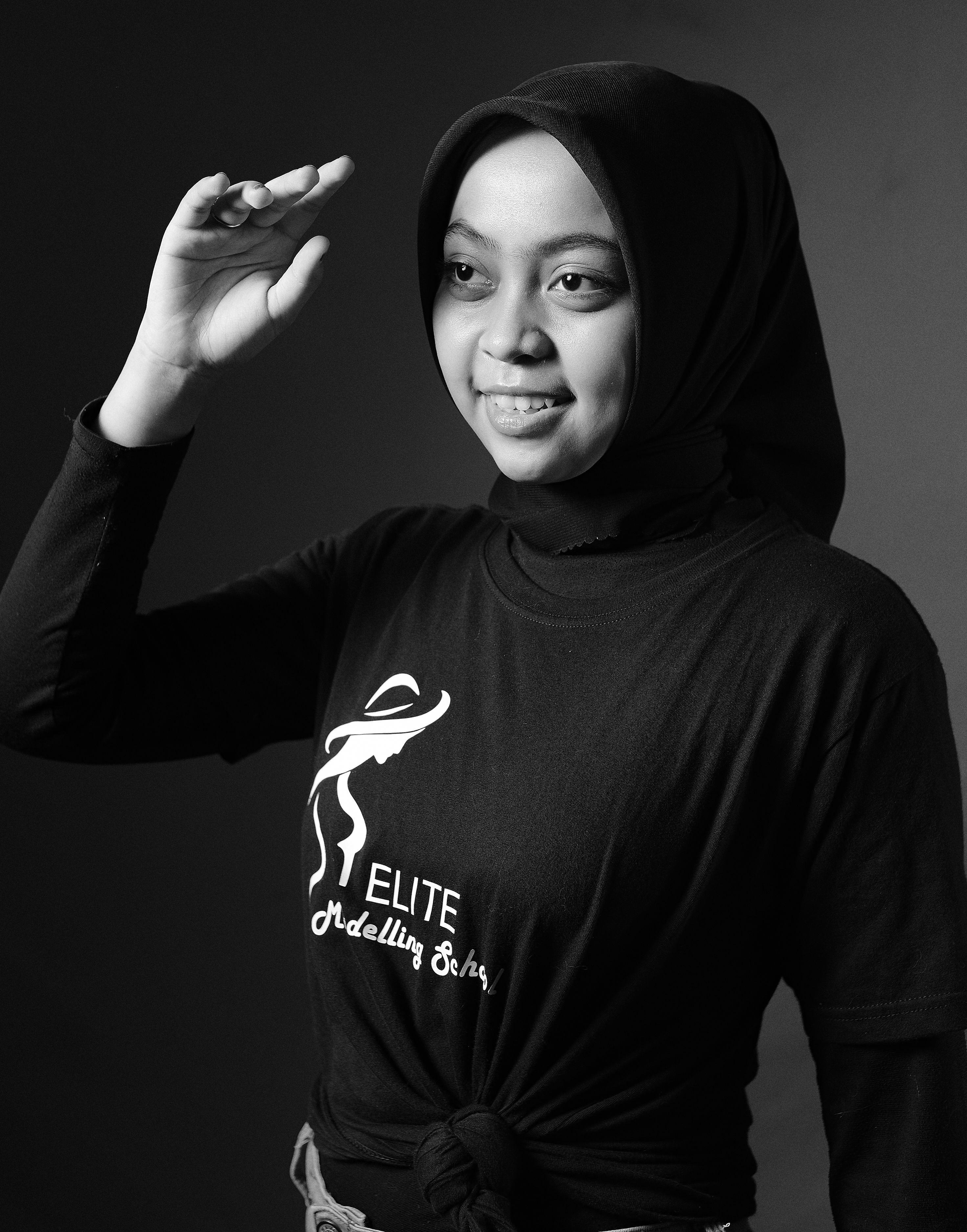 A monochrome studio shot capturing a smiling woman wearing a hijab and a stylish t-shirt in a poised pose.