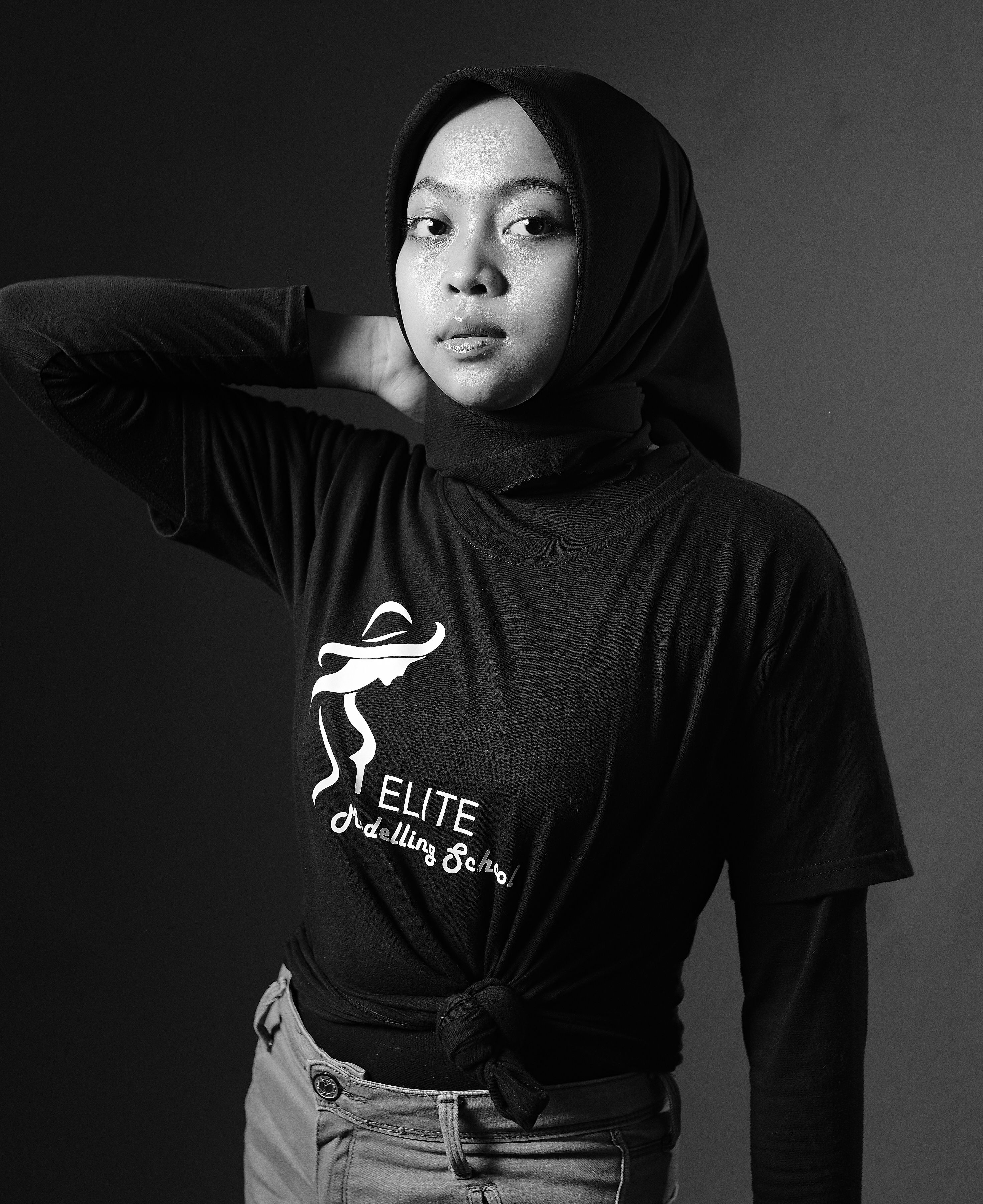 Black and white studio portrait of a woman wearing a hijab, striking a confident pose.
