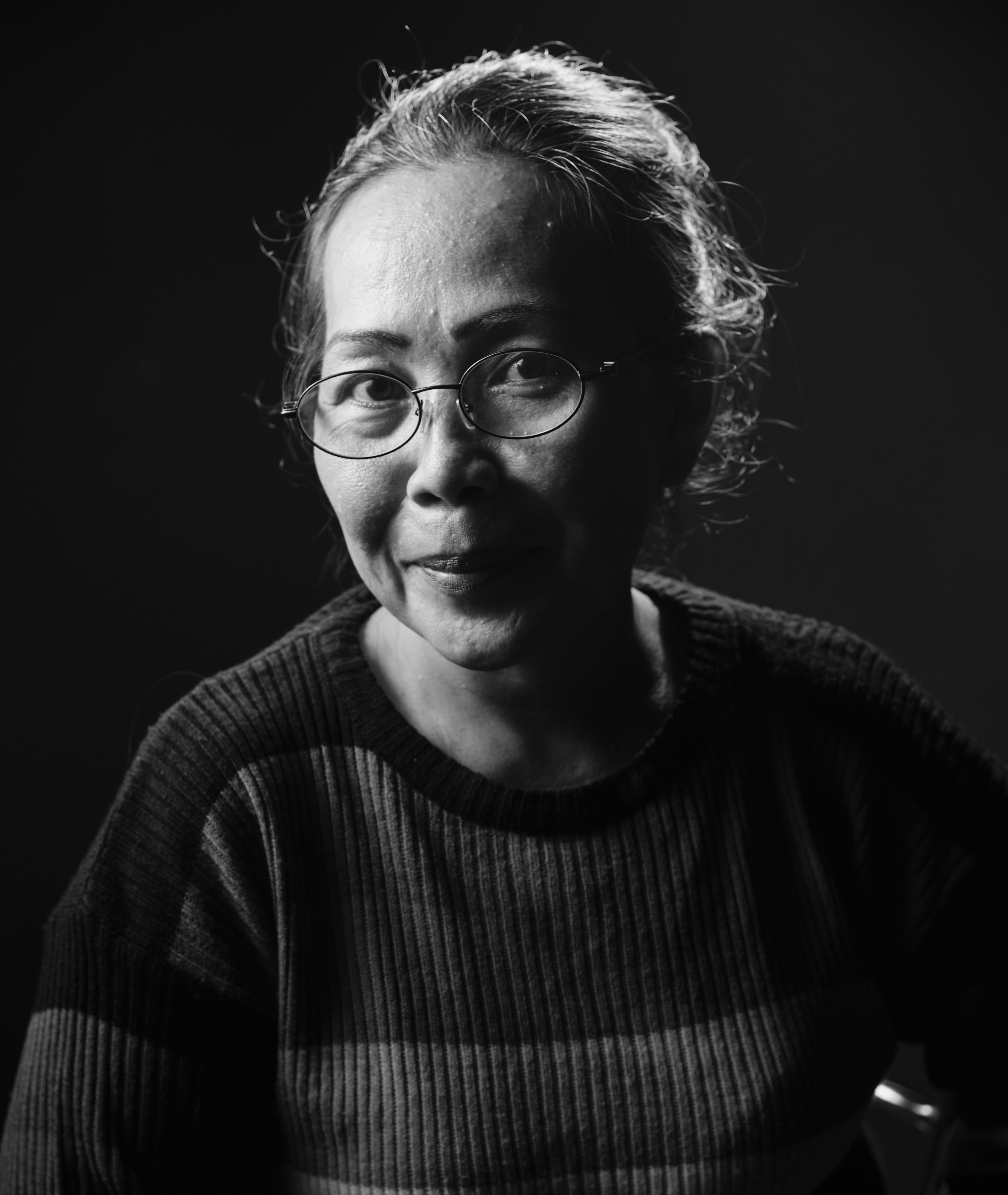 Black and white studio portrait of an Asian woman wearing glasses, captured in a thoughtful pose.