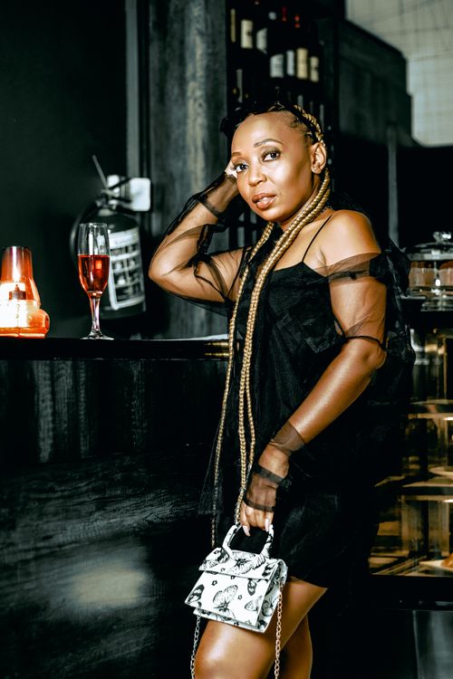 Free Elegant woman with braided hair poses with a glass of wine in a chic bar setting. Stock Photo