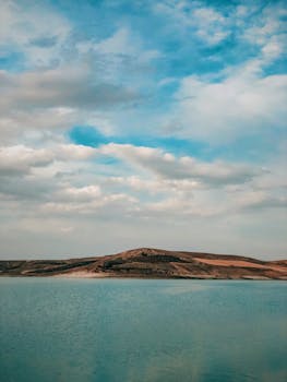 Scenic view of a calm lake with rolling hills under a vibrant blue sky with clouds.