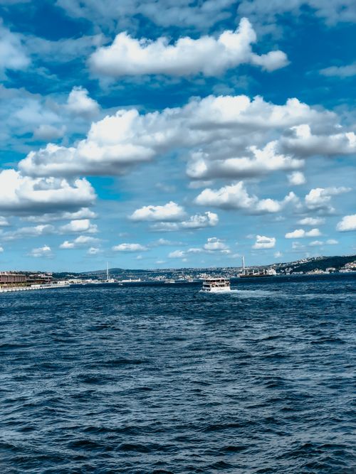 Free A ferry boat sailing on a tranquil sea under a vibrant sky filled with fluffy clouds. Stock Photo