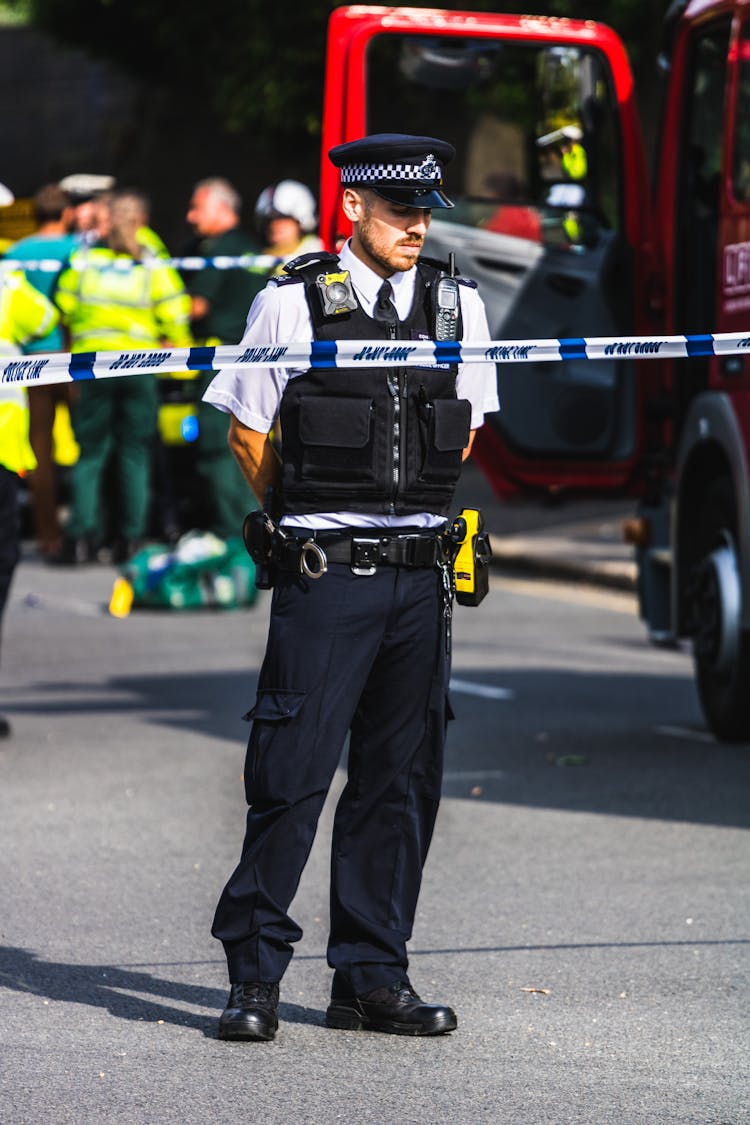 Police Officer Standing Behind A Barricade Tape 