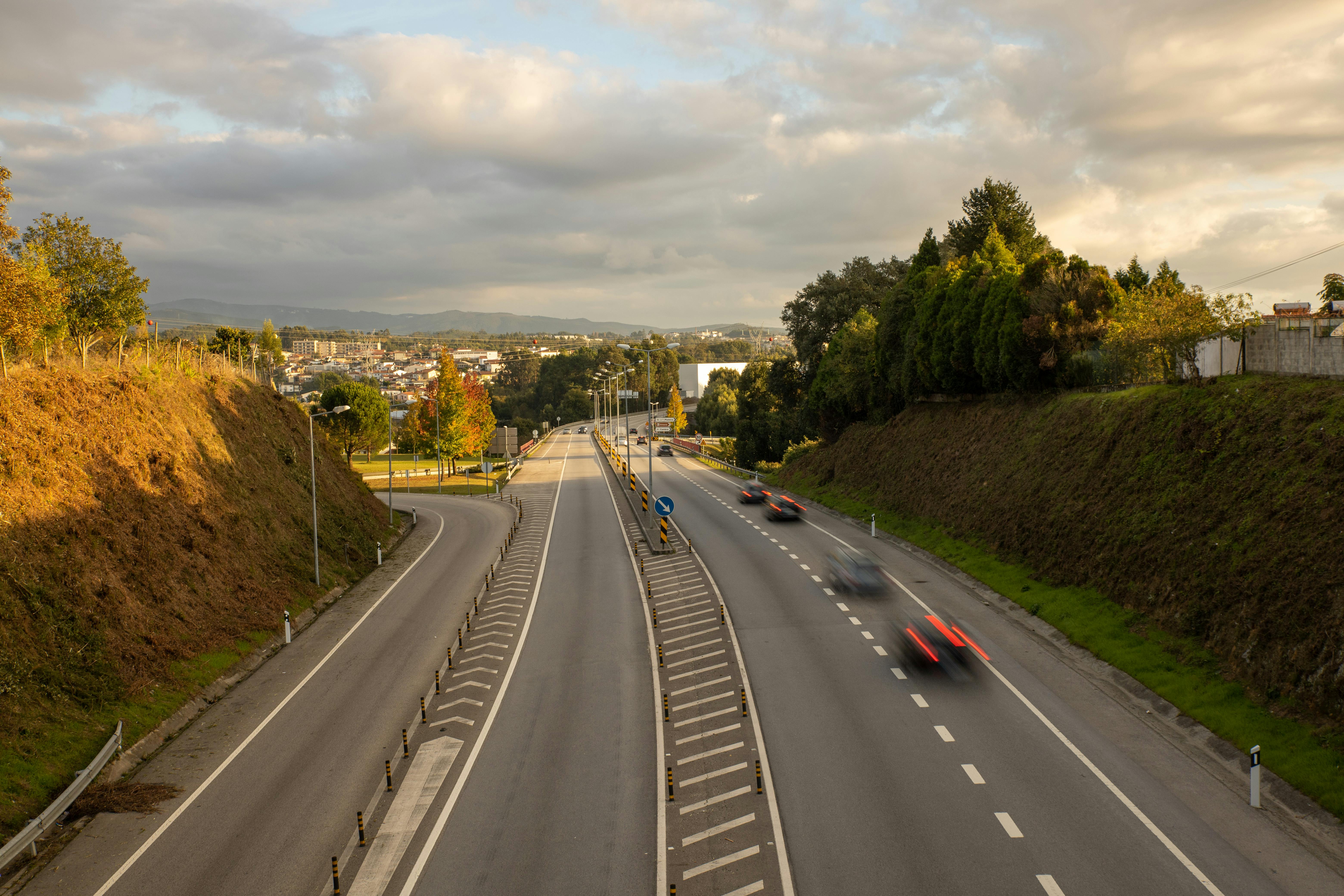 A serene rural highway scene with motion blur vehicles under a cloudy sky.