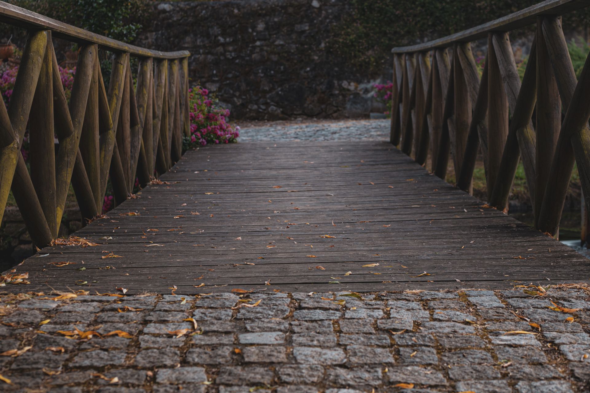 Charming rustic wooden bridge and cobblestone pathway in a lush garden setting.