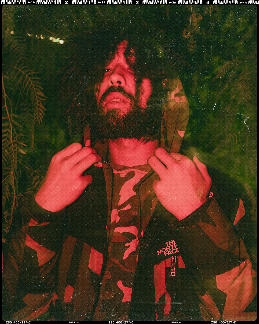 Bearded man in a camouflage jacket posing under red light at night.