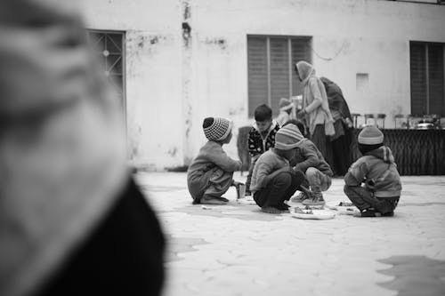 Grayscale Photo of Kids Sitting and Eating on the Floor