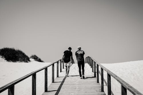 Фотография мужчины и женщины, пересекающих мост в оттенках серого