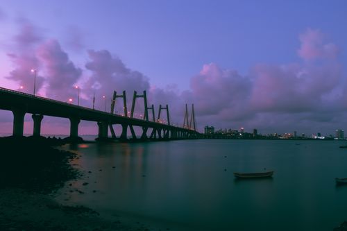 Free A stunning twilight photograph of an architectural bridge over calm waters, with a vibrant city skyline visible in the background. Stock Photo