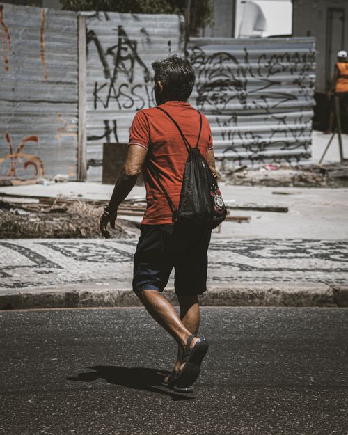 Free A man in casual attire crosses a city street with graffiti in the background, showcasing urban life. Stock Photo