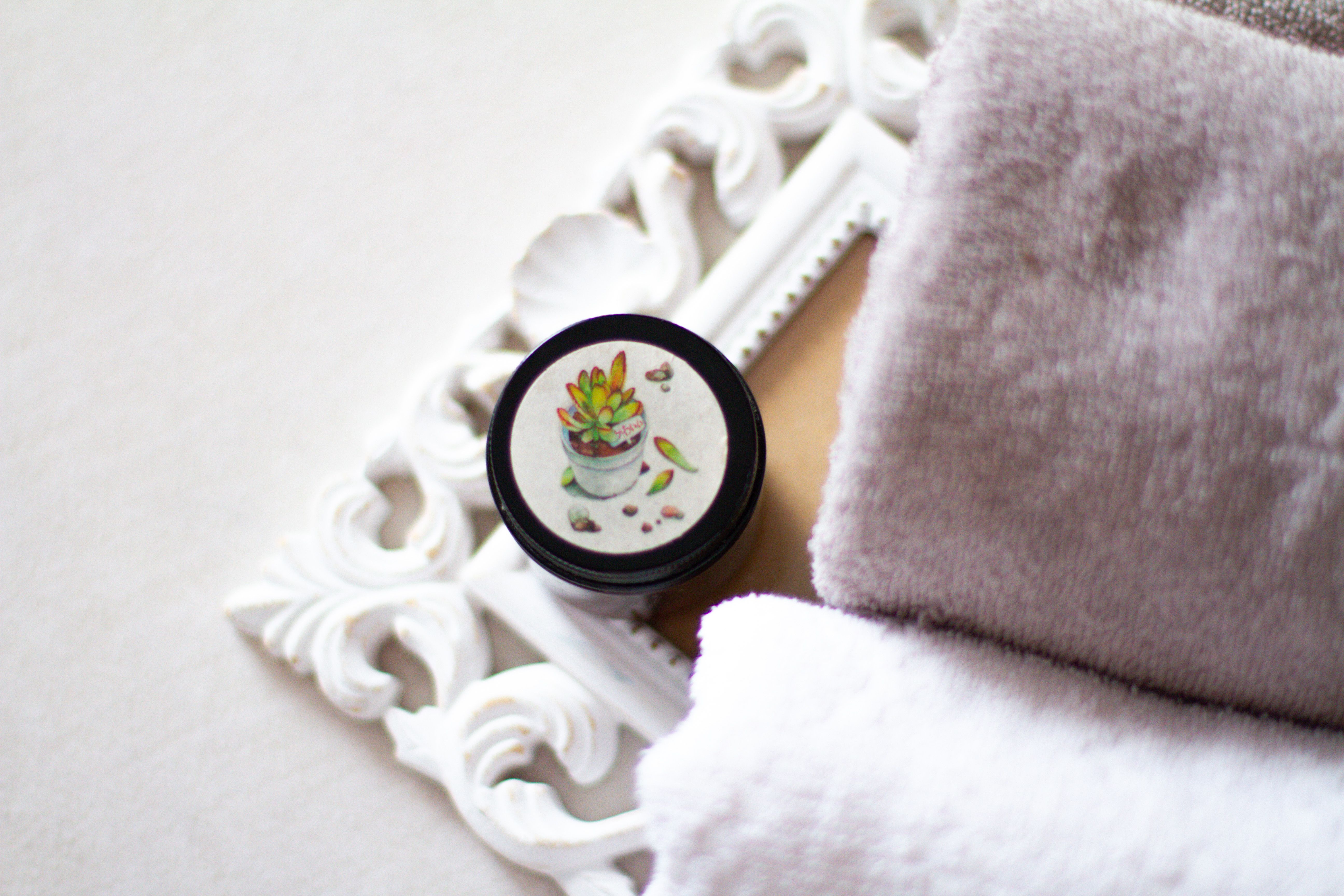 Aesthetic overhead image featuring a succulent-themed jar on a decorative tray with towels.