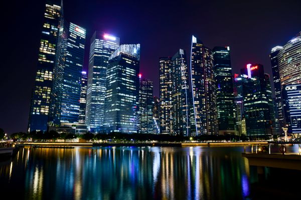 Cativante paisagem noturna da cidade de Cingapura com arranha-céus iluminados refletindo na orla.