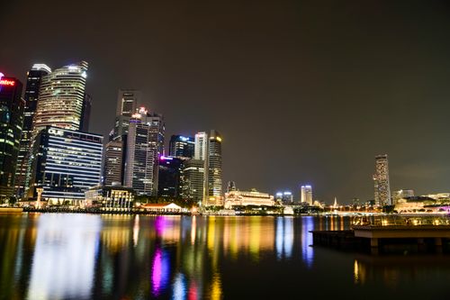 Free Vibrant cityscape of Singapore's illuminated skyline reflecting on the calm waterfront at night. Stock Photo